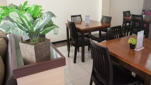 Un comedor con una mesa y sillas de madera, una planta en maceta y un atril para menús.