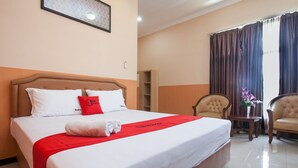 Una habitación de hotel con una cama grande, una manta roja y una almohada roja. Hay una pequeña mesa con un jarrón de flores y dos sillas.