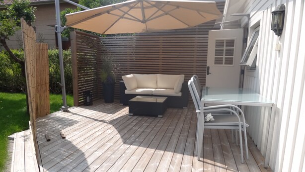 A wooden deck with a sofa and chairs, a table, and a pergola with an umbrella. - Eklanda Studio 51 (Gothenburg)