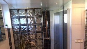 A bathroom with a large mirror, a sink, a shower with a glass partition, and dark tiled flooring. - Eklanda Studio 51 (Gothenburg)
