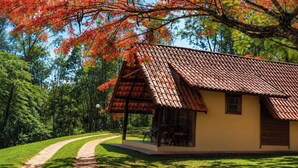 A small house with a tiled roof, a porch with chairs, and a pathway leading to it. - Hotel Fazenda Menino da Porteira (Ouro Fino)