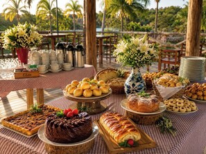 A buffet table with various baked goods, a chocolate cake, and a floral centerpiece. - Hotel Fazenda Menino da Porteira (Ouro Fino)