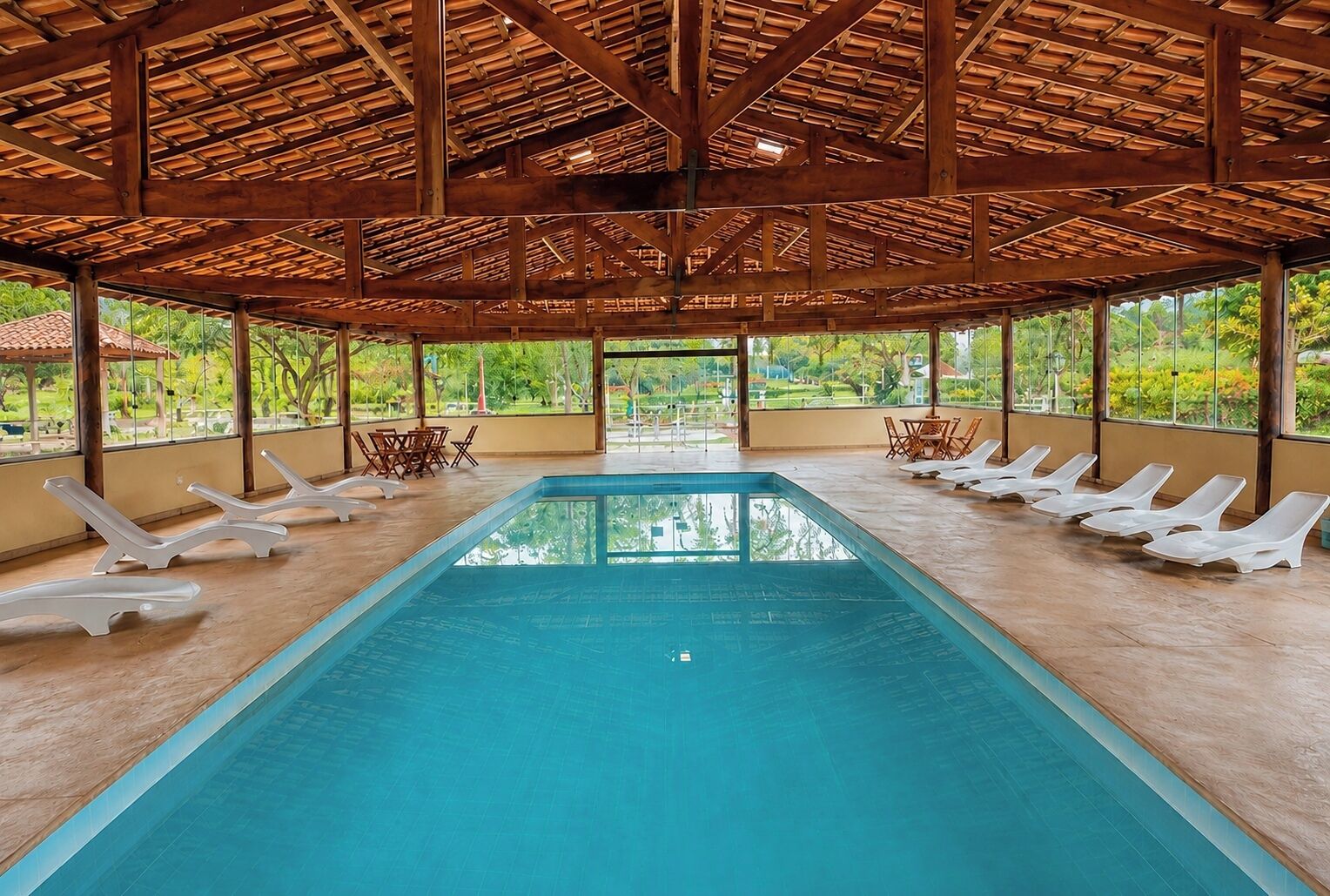 Une piscine avec des chaises longues, un espace couvert avec des poutres en bois et une vue sur la verdure environnante.