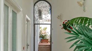 Un couloir avec une porte blanche, un portail en métal et un escalier menant à un espace extérieur agrémenté de plantes.