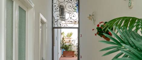 Un couloir avec une porte blanche, un portail en métal et un escalier menant à un espace extérieur agrémenté de plantes.