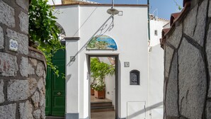 Une rue étroite bordée d’un immeuble blanc, avec une porte verte et un petit porche.
