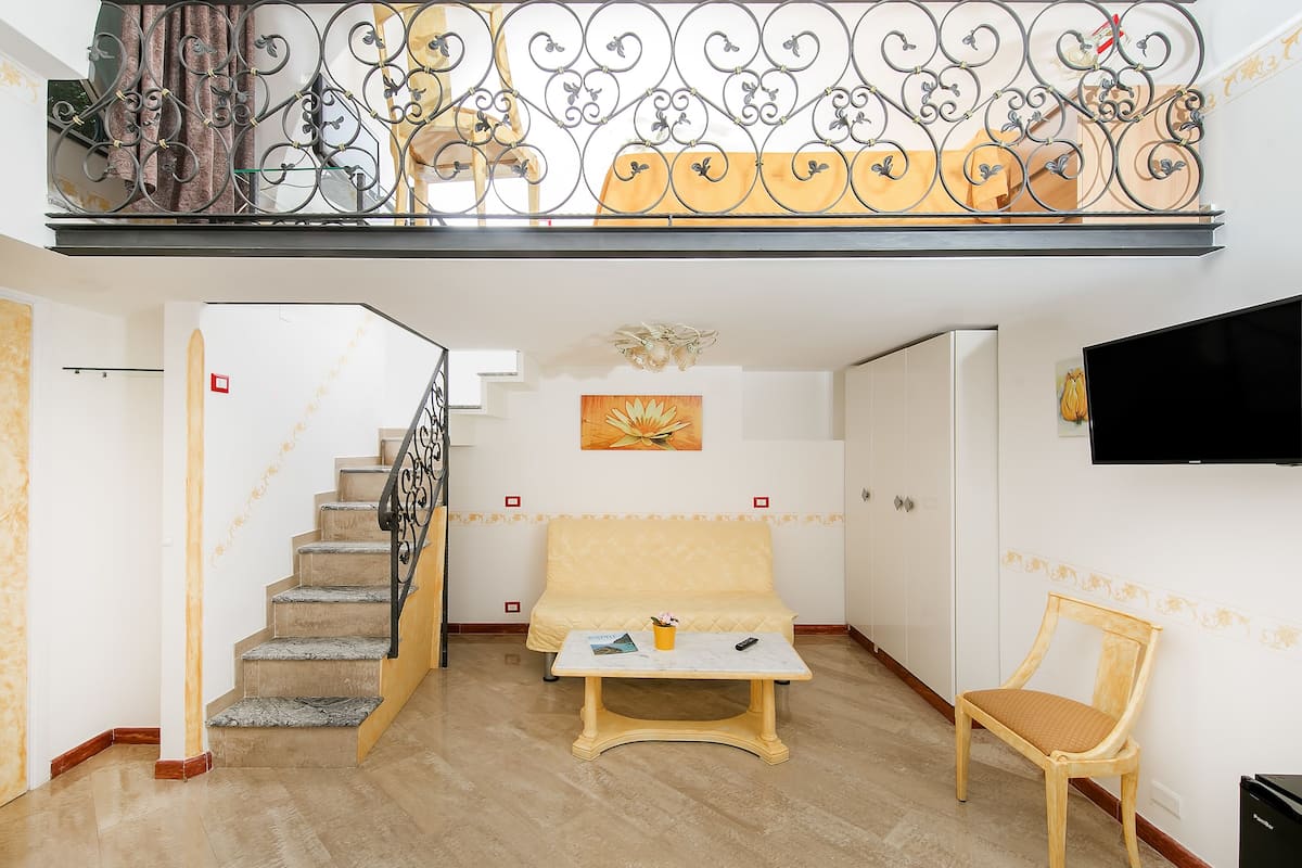 Amplia sala de estar con una escalera, un sofá, una mesa de centro y un televisor instalado en la pared.