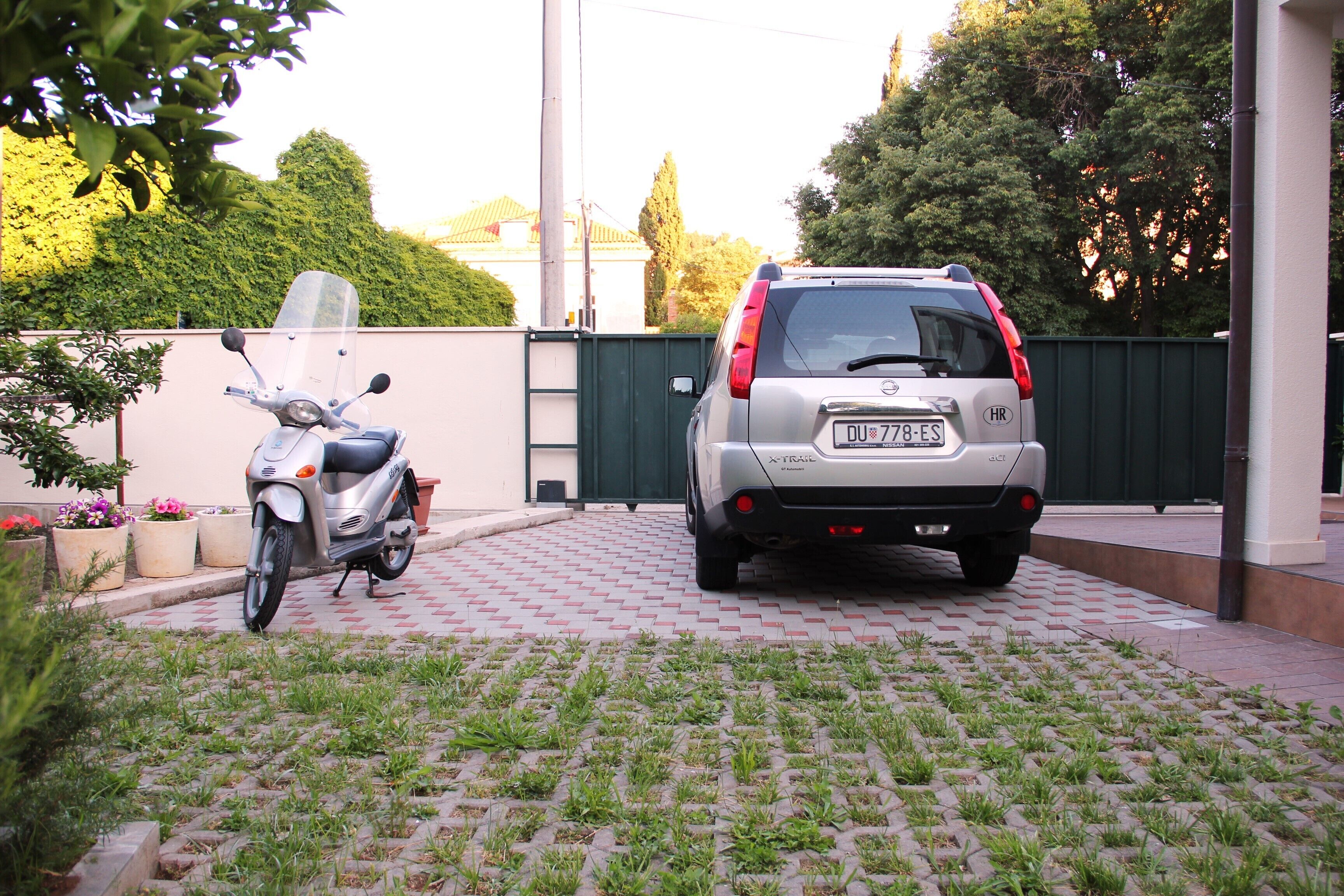 A paved driveway with a parked scooter and a car.
