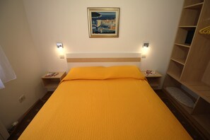A hotel room with a single bed, two bedside tables, a nightstand, a wooden wardrobe, and a framed picture on the wall.