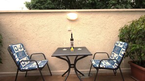 Un pequeño patio exterior con una mesa y dos sillas, una planta en maceta y un aplique de pared.