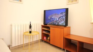 Una habitación con televisión sobre un soporte de madera, una mesita con botella de vino y copa, y un radiador.
