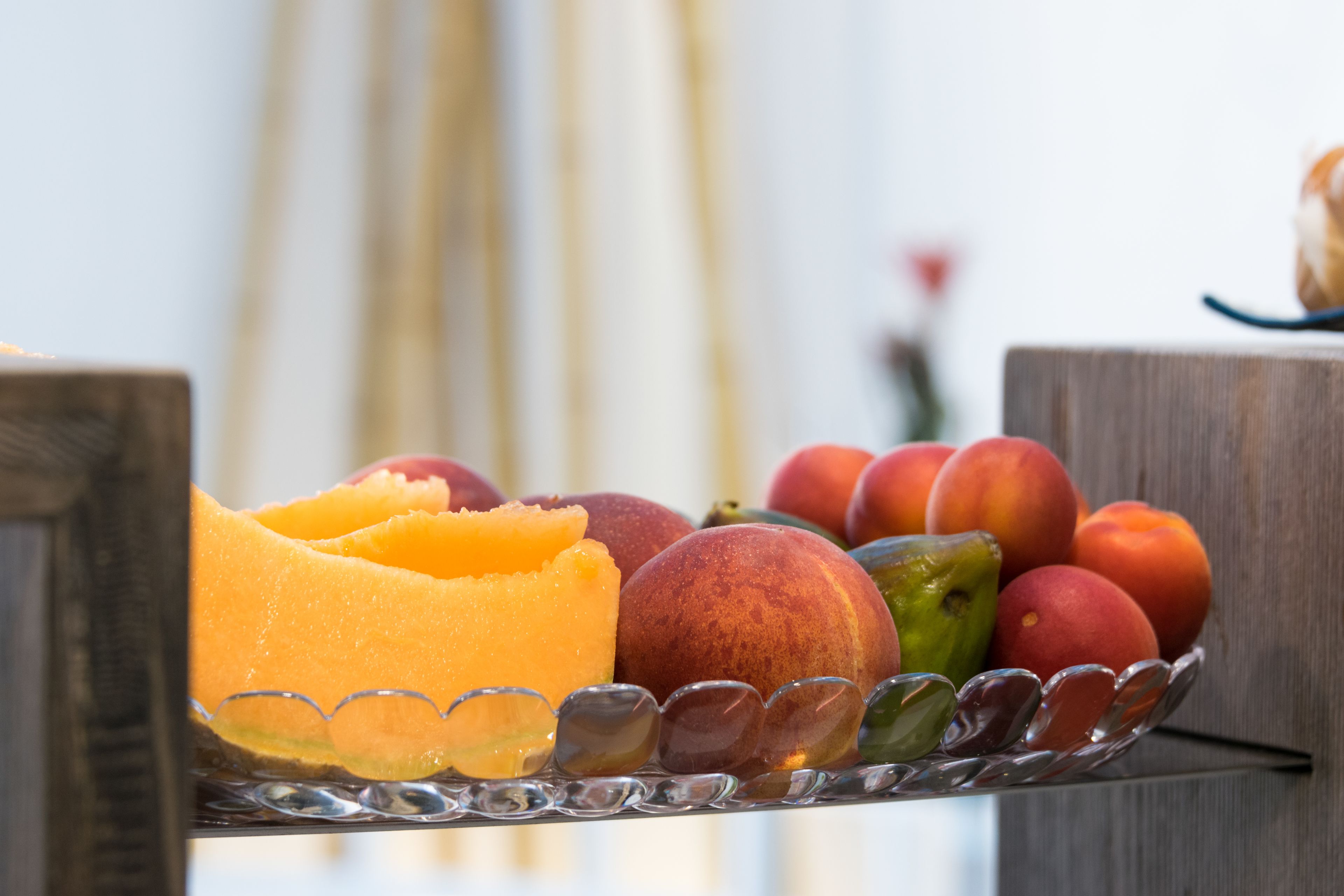 Un saladier en verre contenant des pêches, des nectarines et un melon sur une table en bois.