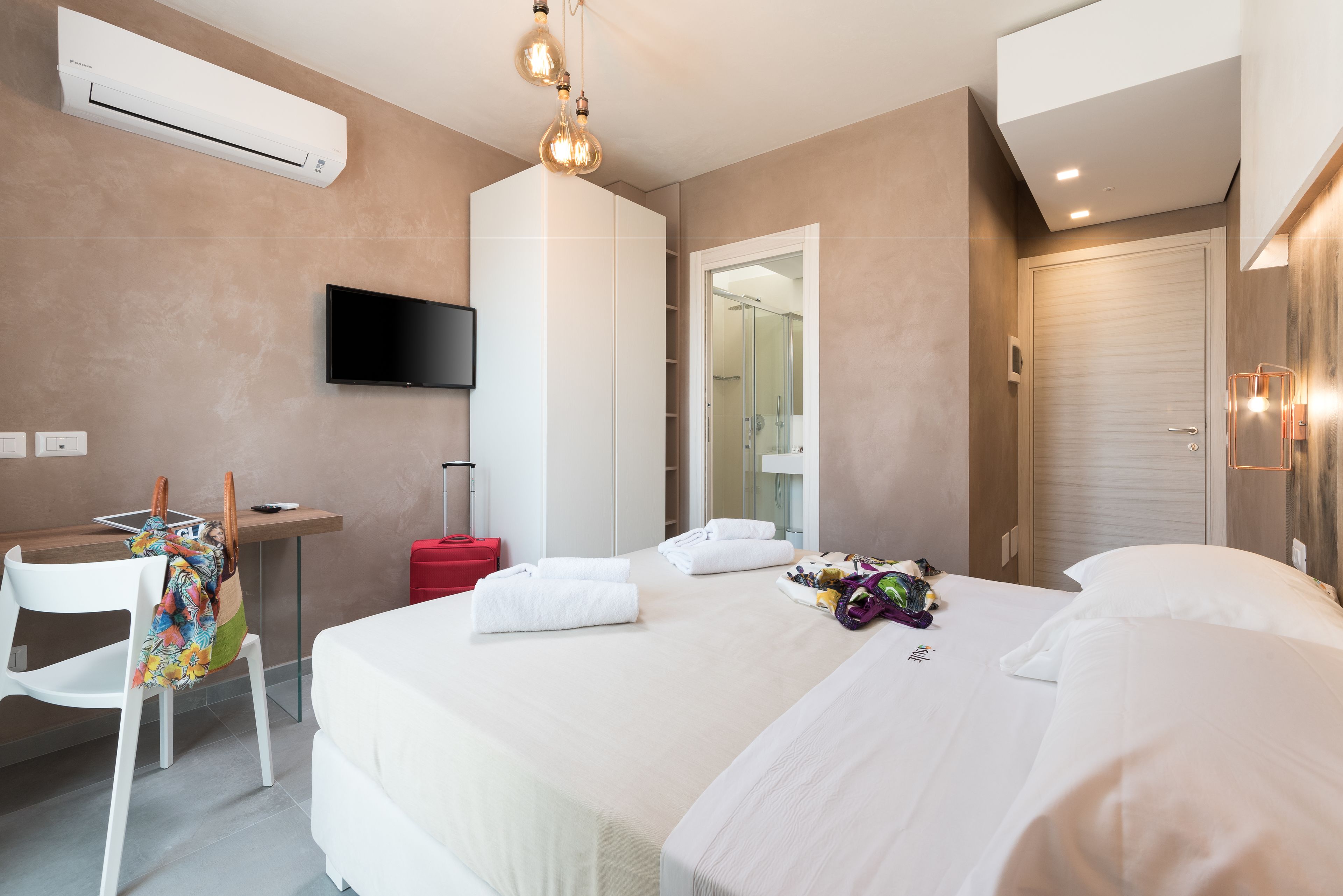 Ein Hotelzimmer mit Bett, Schreibtisch, Stuhl, Fernseher und Klimaanlage.