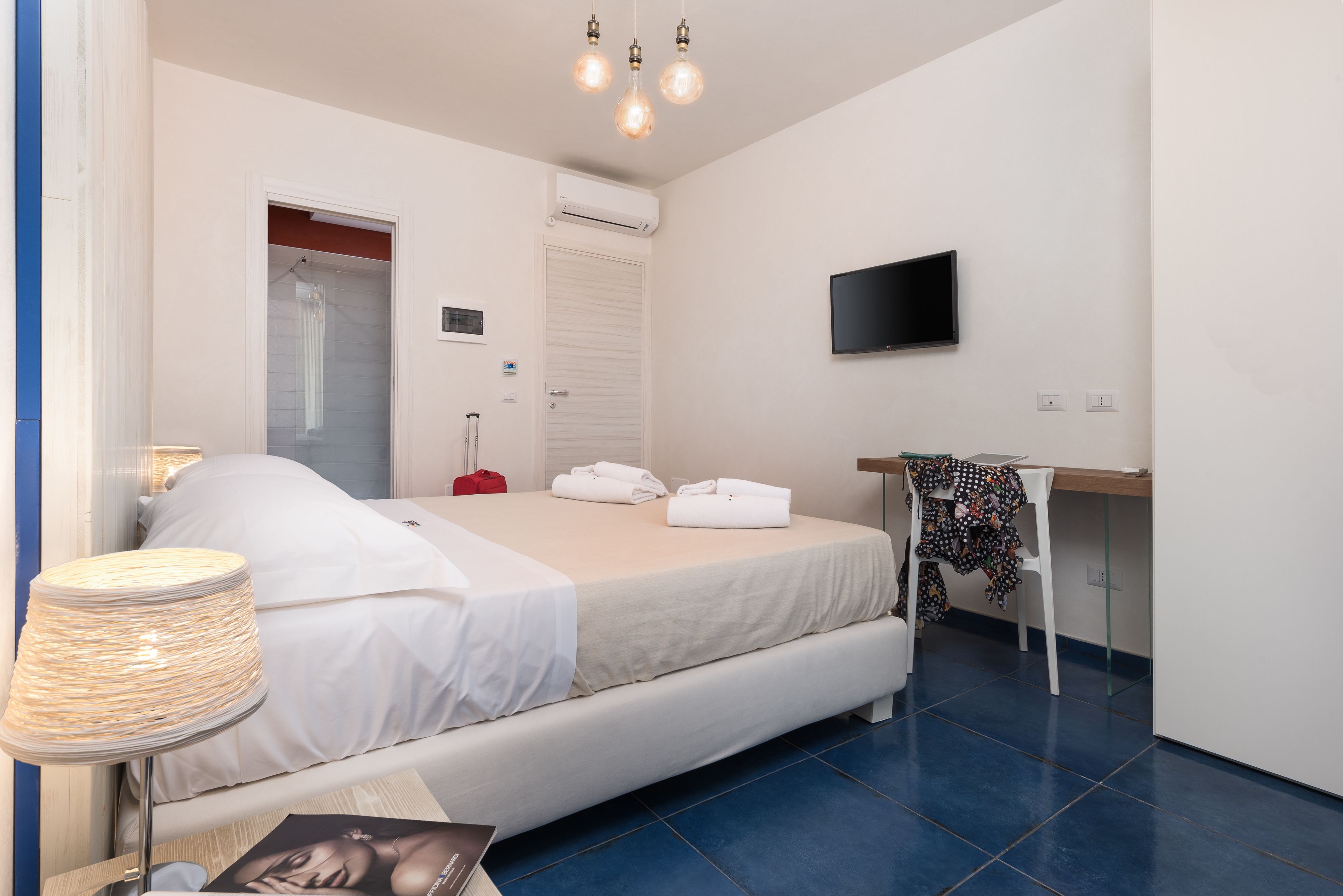 A bedroom with a bed, a desk, a TV, and an air conditioning unit.