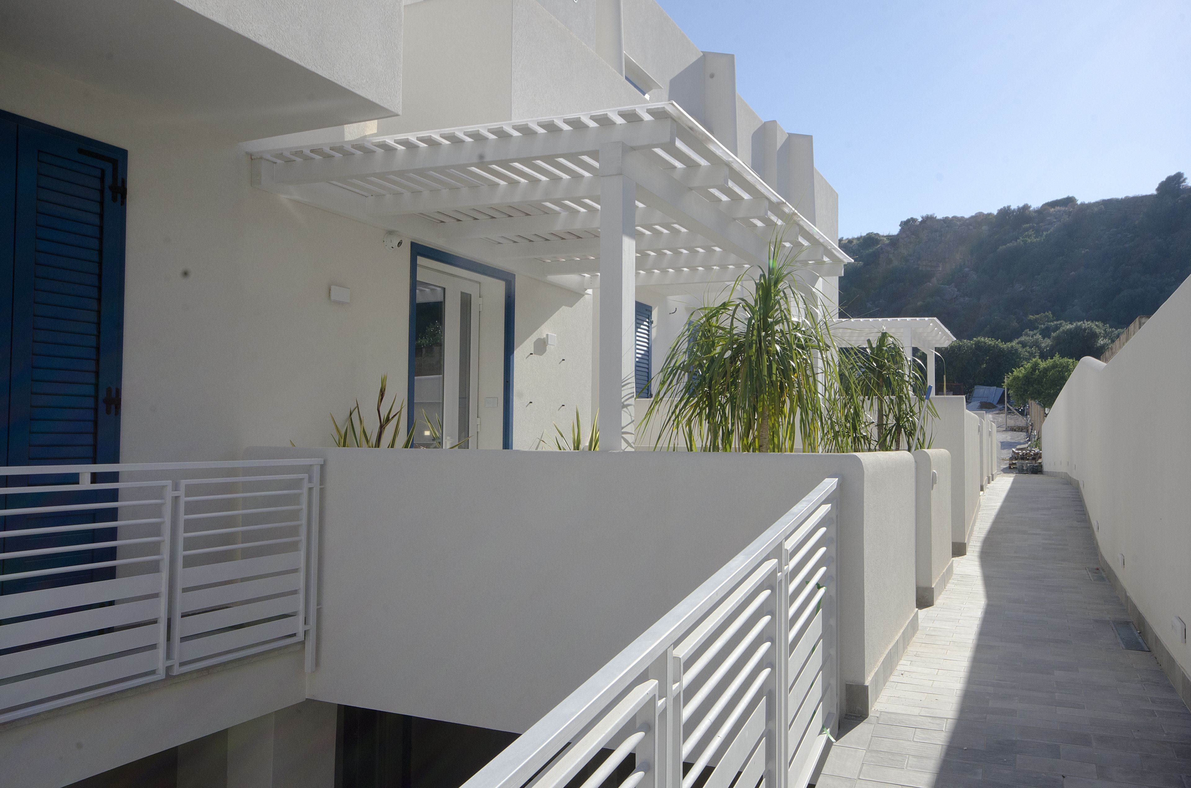 A narrow, covered walkway with white railings, leading to a building with a blue door and shutters.