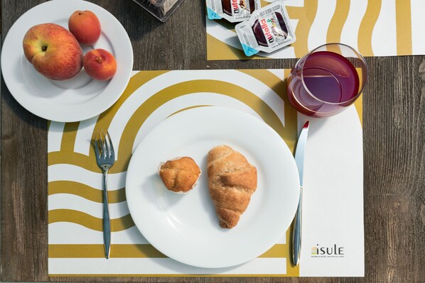 A breakfast setting with a plate of peaches, a glass of juice, and two croissants on a table with a striped placemat.