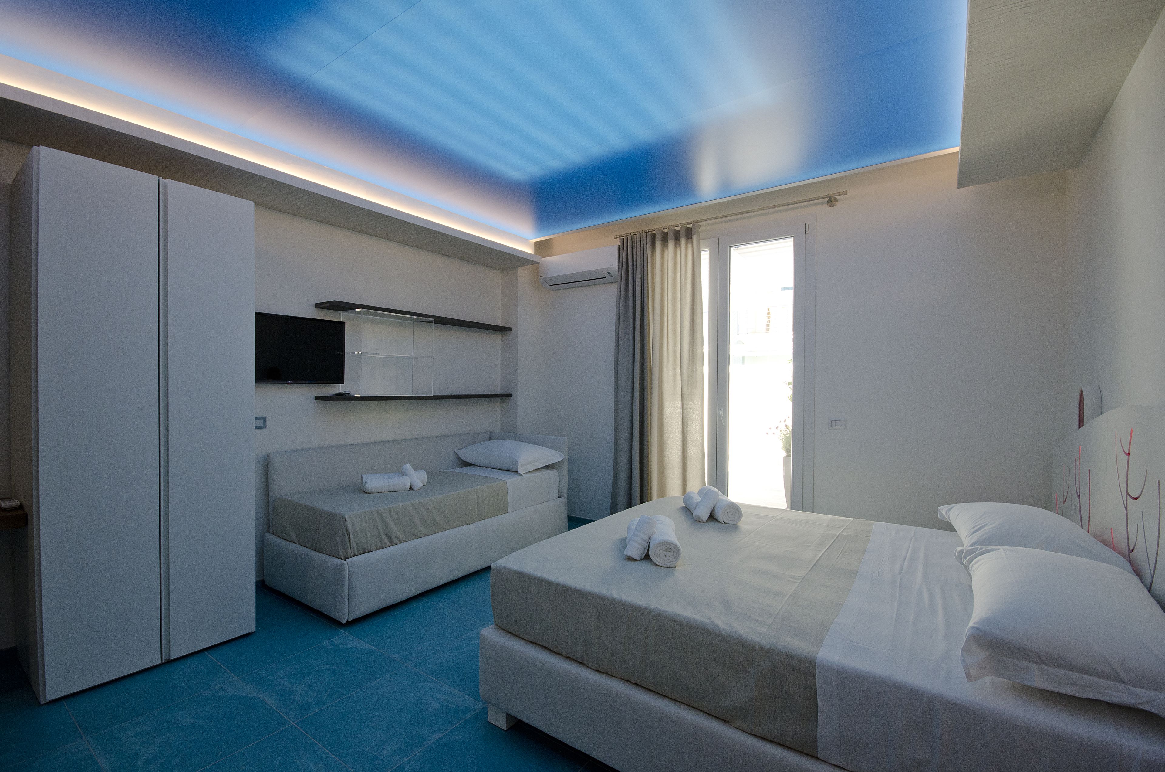 A modern hotel room with a large bed, a smaller bed, a wardrobe, and a television.