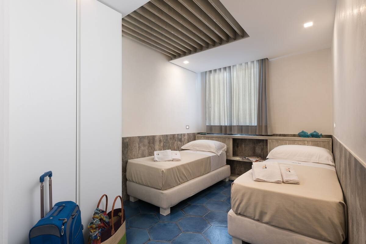 A hotel room with two beds, a suitcase, a handbag, and a window with curtains.
