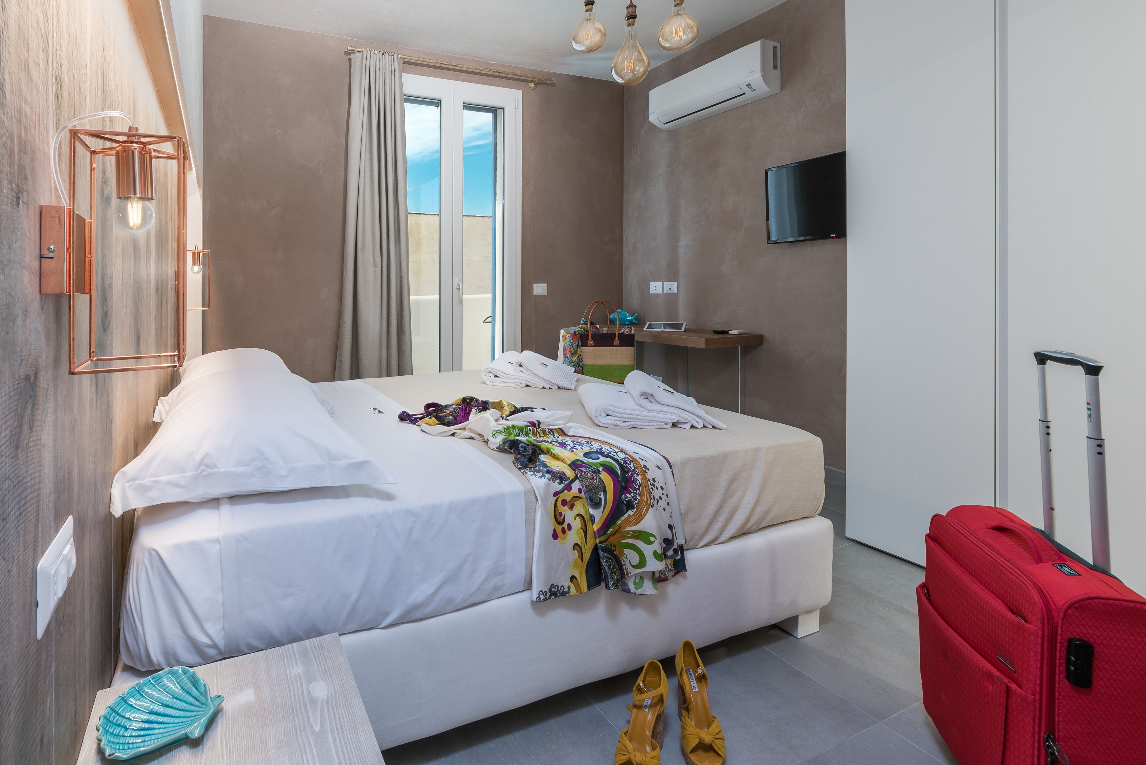 Una camera d'albergo con un letto, una scrivania, un televisore e una valigia.