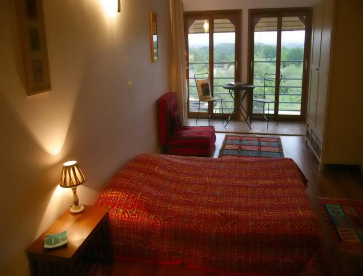 Un dormitorio con una cama grande, una silla, una mesita de noche con lámpara y un balcón con vistas.