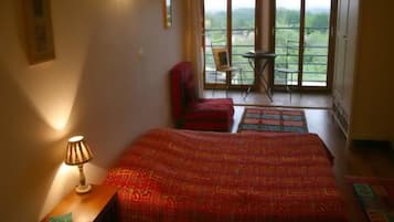 Un dormitorio con una cama grande, una silla, una mesita de noche con lámpara y un balcón con vistas.
