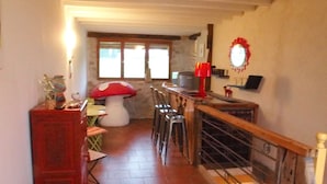 Una cocina acogedora con una escalera de madera, una zona de comedor con una mesa con forma de hongo y una lámpara roja en la encimera.