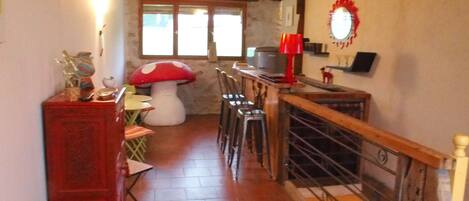 Une cuisine chaleureuse avec un escalier en bois, un coin repas doté d’une table en forme de champignon et une lampe rouge posée sur le comptoir.