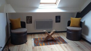 Una habitación pequeña y moderna con tragaluz, dos sillones, una mesa de centro de vidrio y un televisor de pantalla plana montado en la pared.