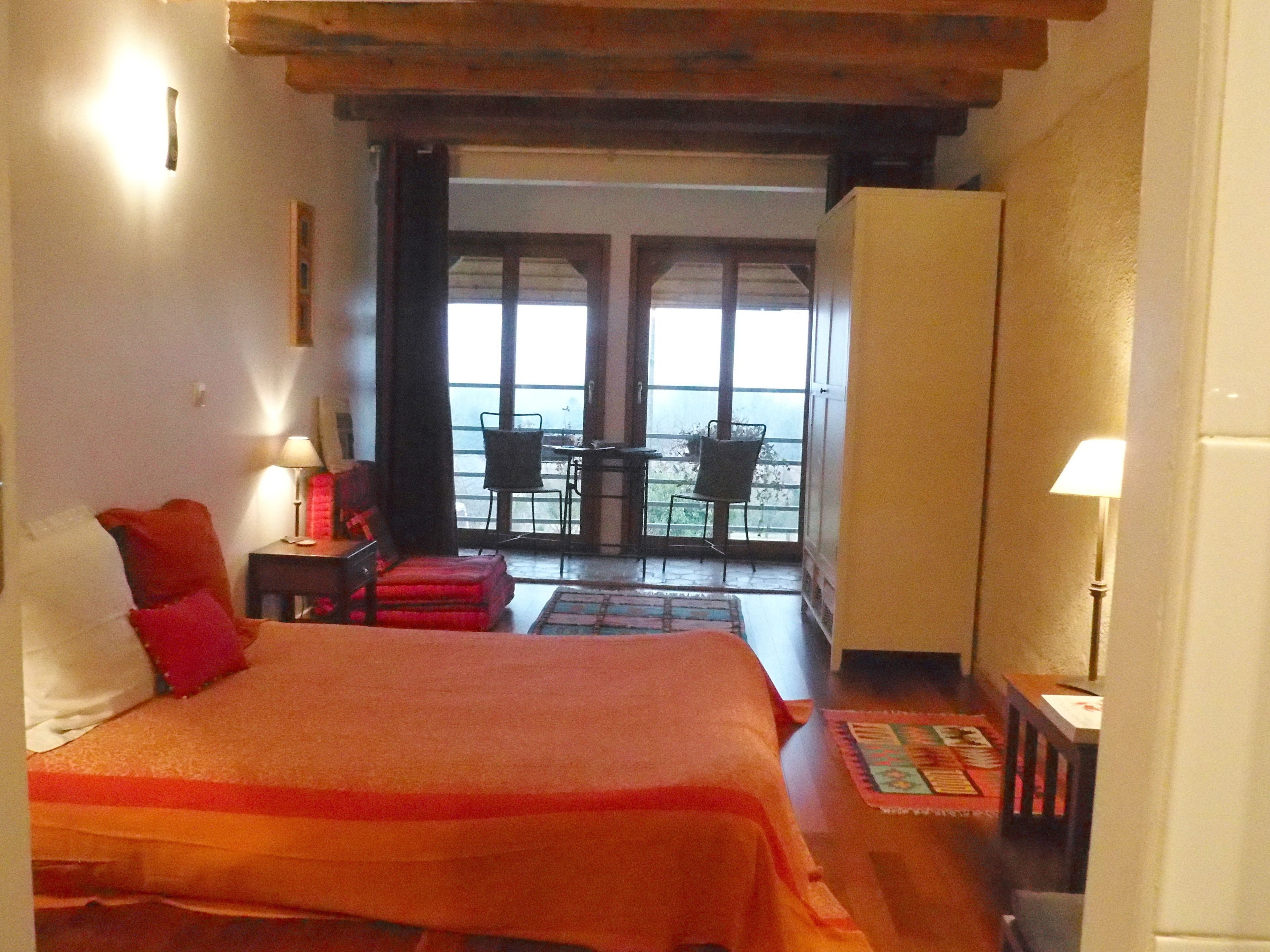 A bedroom with a large bed, a desk, a chair, and a balcony with a table and chairs.