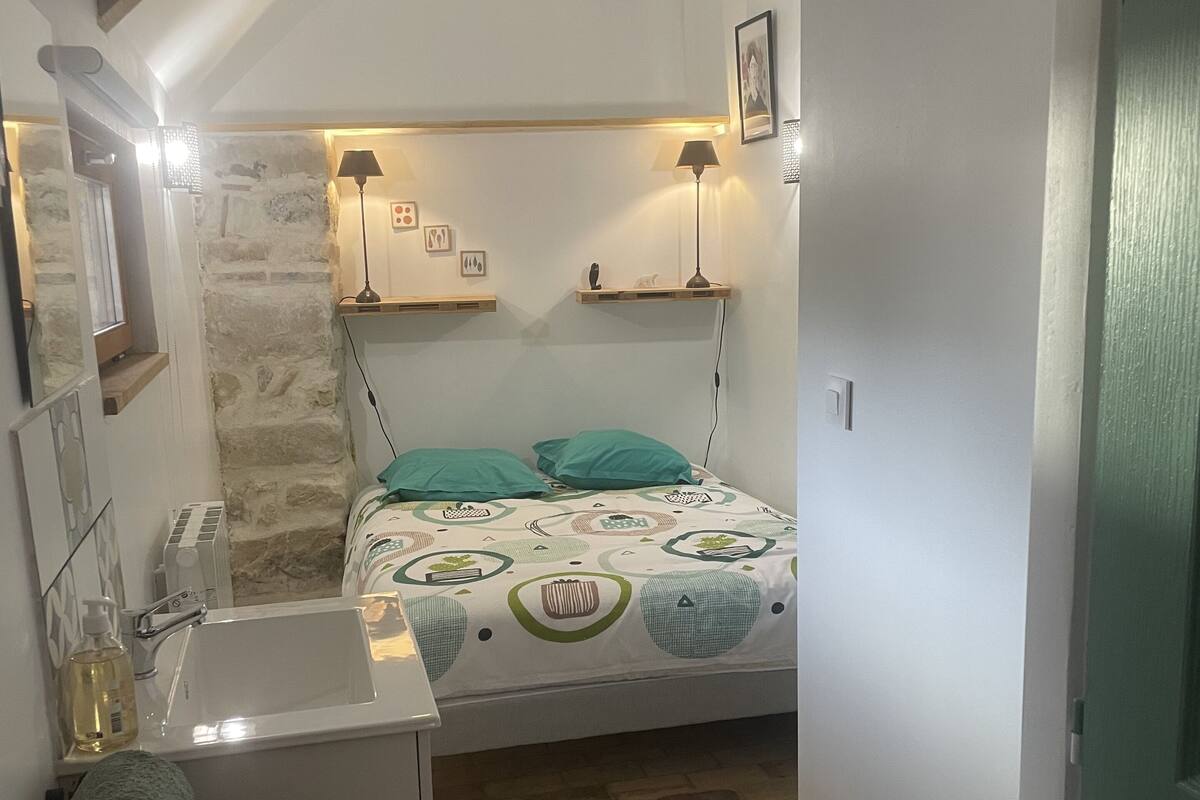 A small, cozy bedroom with a bed, bedside lamps, a nightstand, and a built-in shelf.
