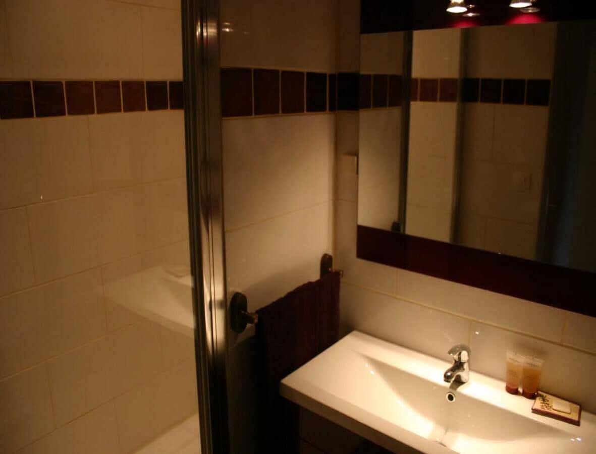 Un bany amb un lavabo blanc, un mirall i un espai de dutxa de vidre.