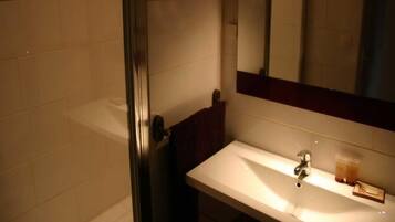 Un bany amb un lavabo blanc, un mirall i un espai de dutxa de vidre.