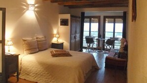 Un dormitorio con cama, lámparas de noche, una mesita y vista al exterior por una puerta.