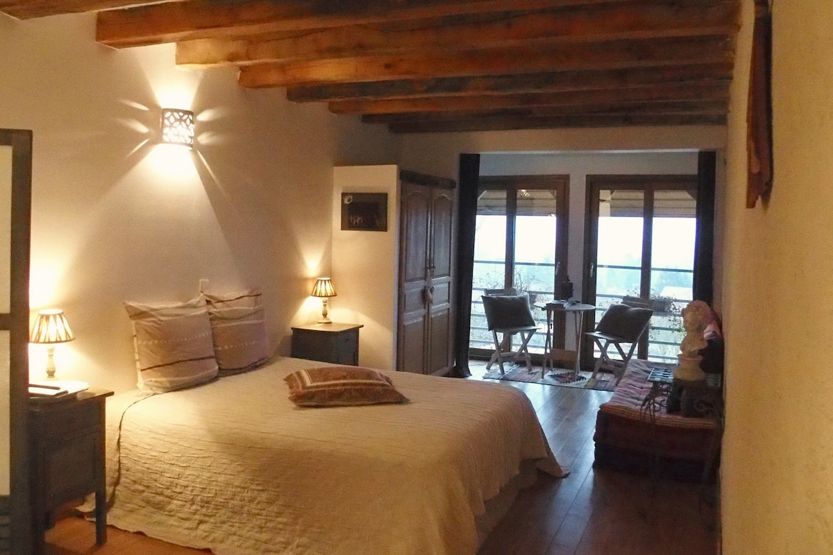 A bedroom with a bed, bedside lamps, a small table, and a view of the outside through a door.