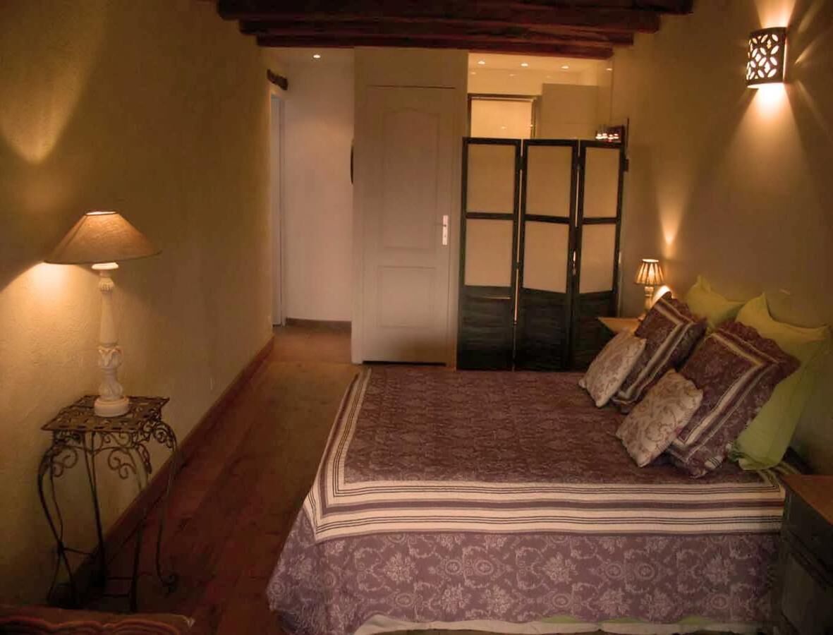 A bedroom with a bed, bedside lamps, and a door leading to another room.