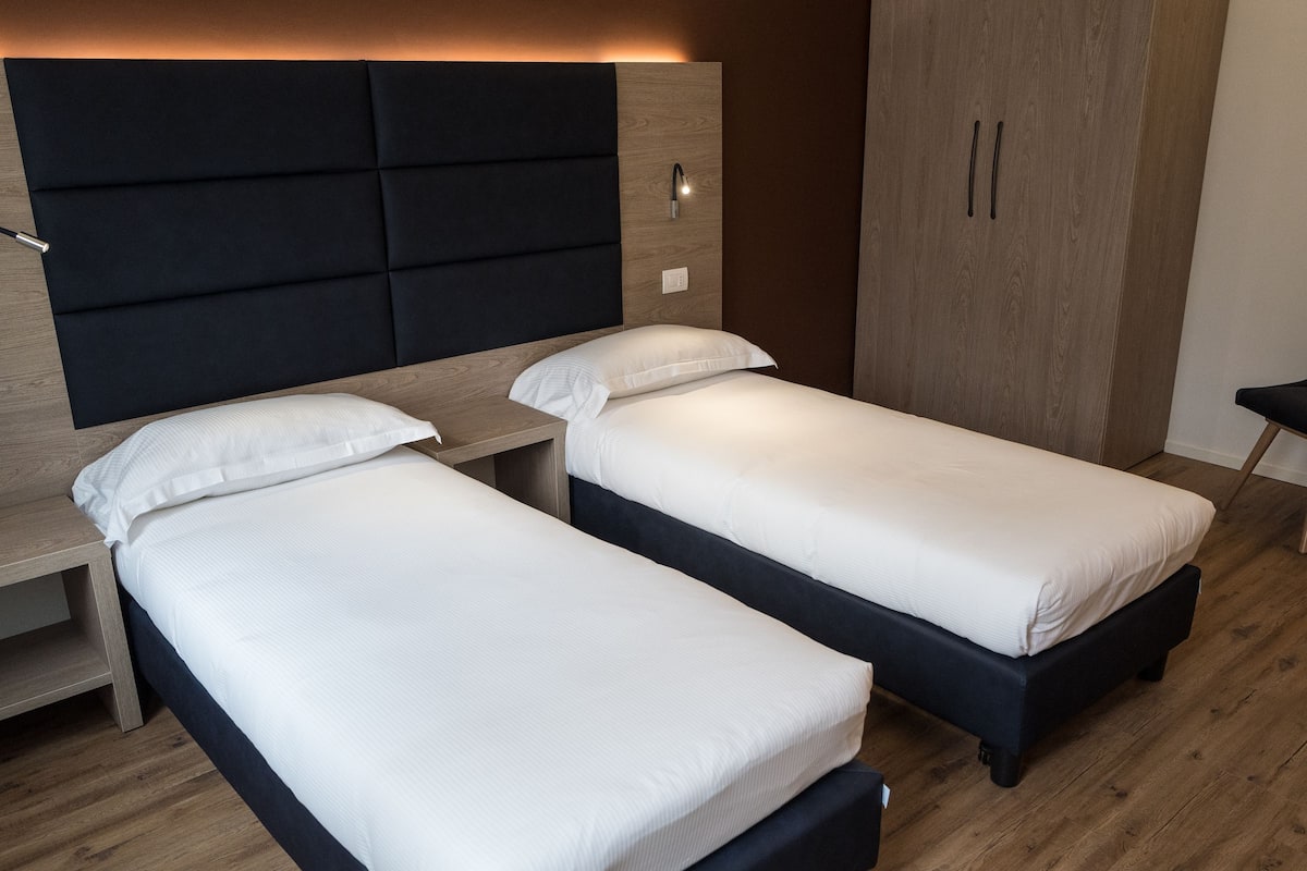 Une chambre moderne avec deux lits simples, une armoire en bois et une table de chevet.