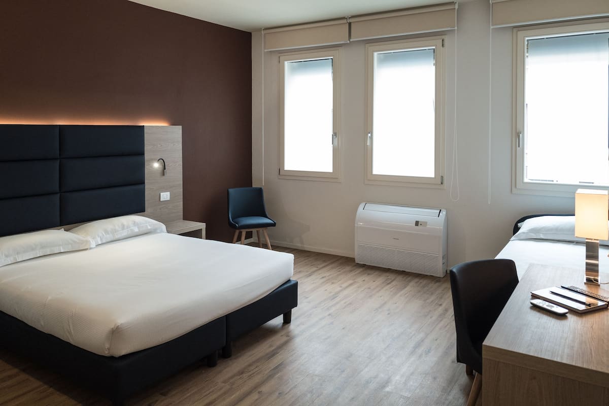 Une chambre d’hôtel équipée d’un lit, d’un bureau, d’une chaise, d’un radiateur et de deux fenêtres.