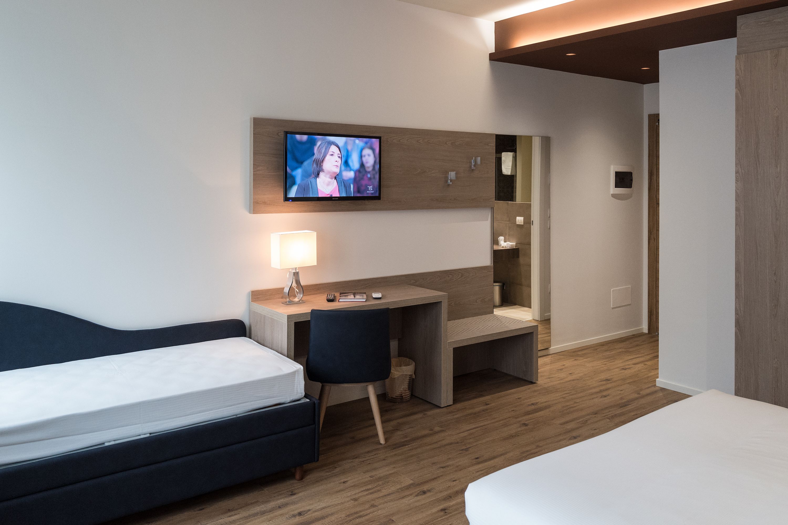 Una habitación de hotel moderna con cama, escritorio, silla, televisor y suelo de madera.