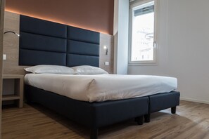 A modern bedroom with a dark headboard, a bedside table, and a window with a view of buildings. - Letto A Castello (Ferrara)
