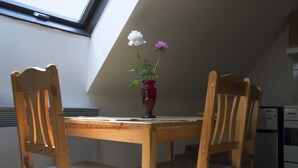 A wooden dining table with two chairs, a red vase with flowers, and a kitchen area with a refrigerator. - Red Point (Tabor)