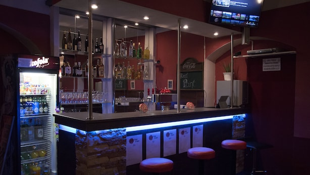A bar area with a refrigerator stocked with beverages, shelves with bottles, and a television mounted above the bar. - Red Point (Tabor)