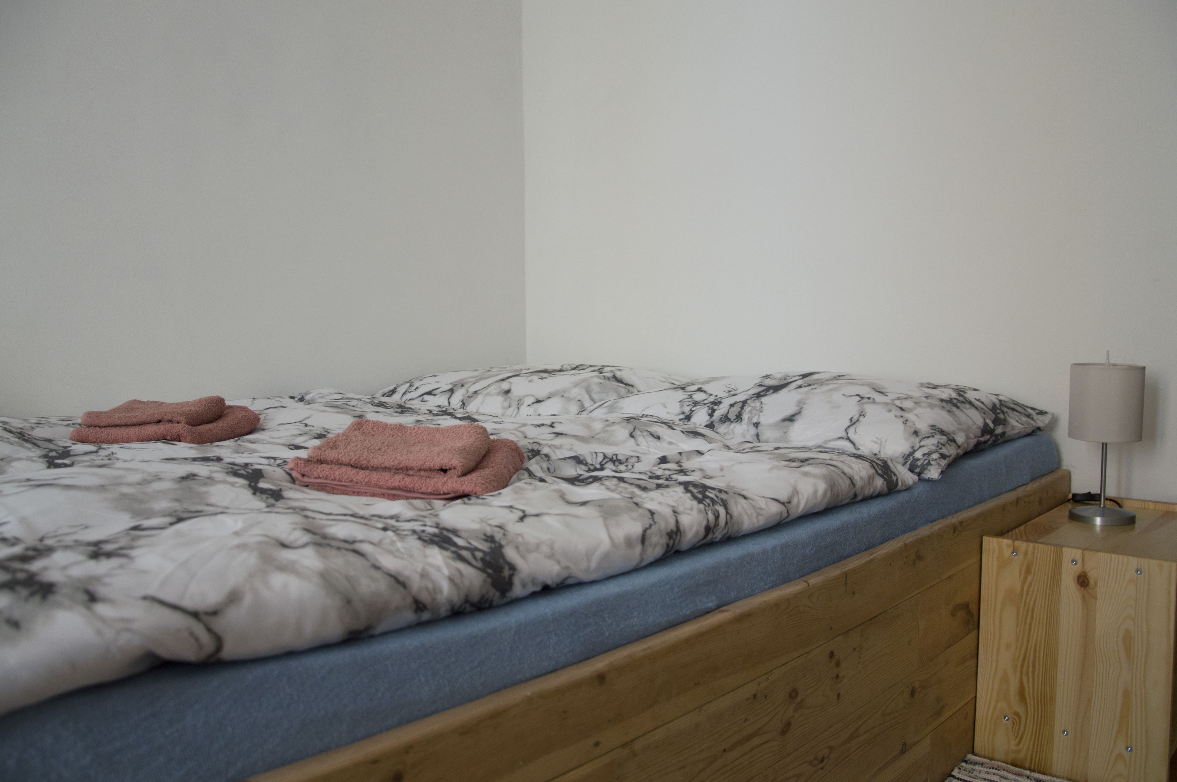 A bed with a marble-patterned bedspread, a blue mattress, and pink towels folded on it.