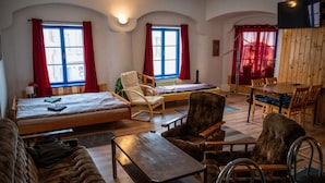 A cozy room with a bed, a sofa, a dining table with chairs, and a TV mounted on the wall. - Red Point (Tabor)