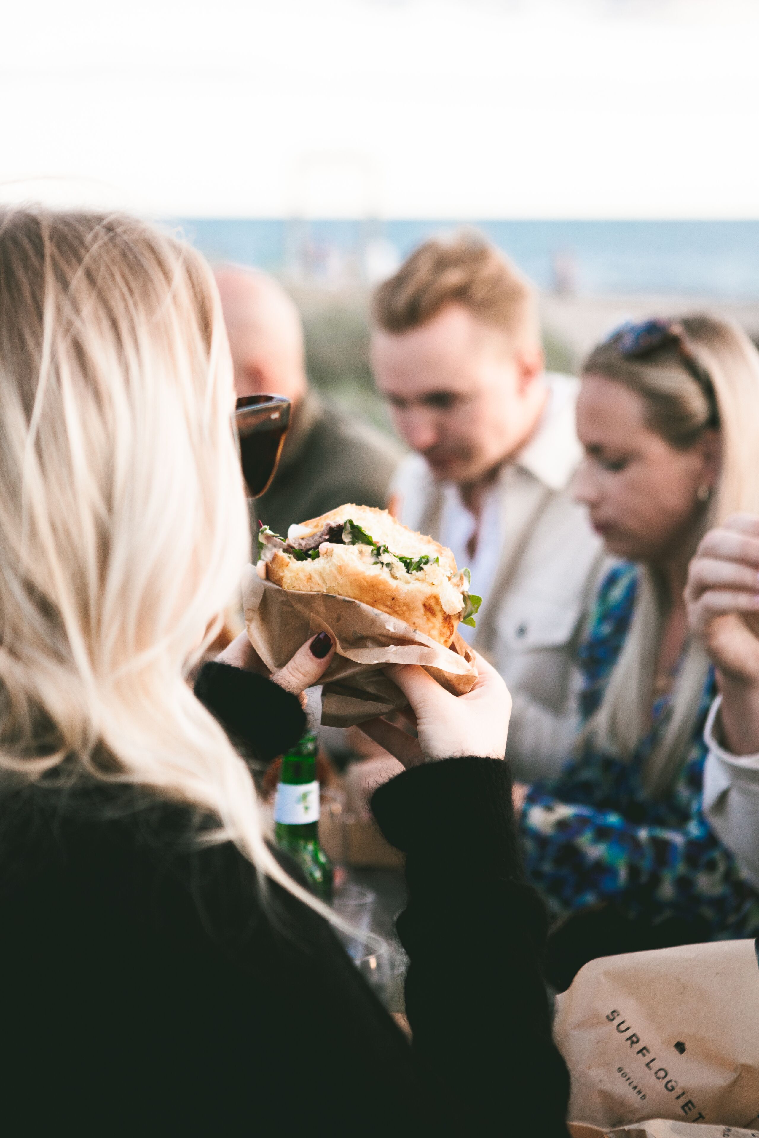A person holding a sandwich at a table with a view of the ocean.