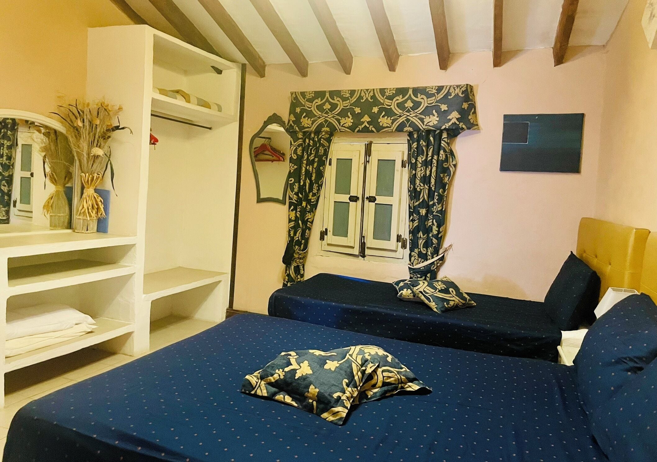 Un dormitorio con dos camas, un armario, una ventana con cortinas y un espejo.