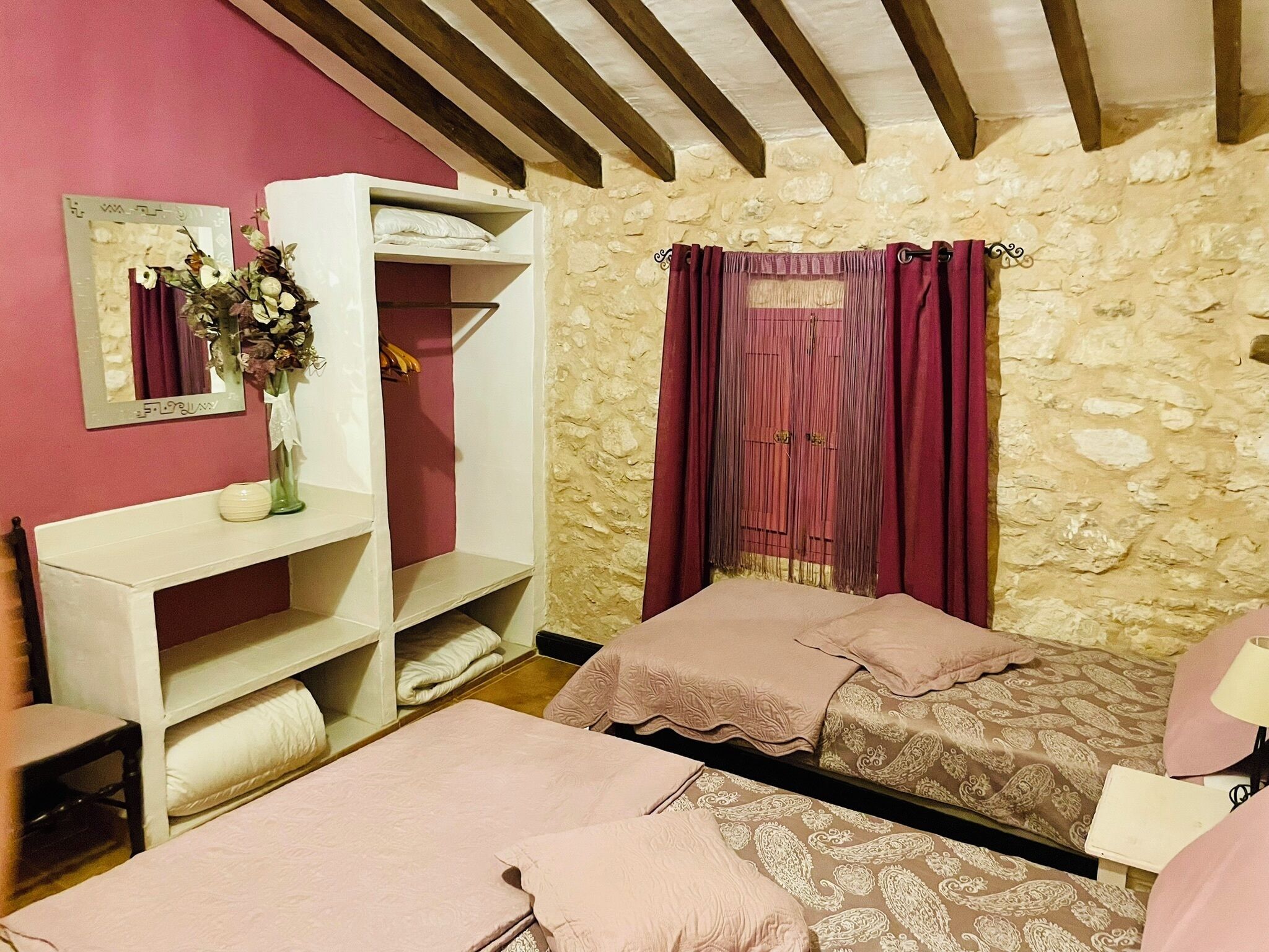 Un dormitorio con dos camas, un tocador con espejo, un aparador y una pared de piedra.