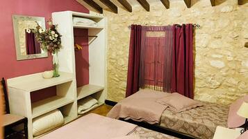 Un dormitorio con dos camas, un tocador con espejo, un aparador y una pared de piedra.