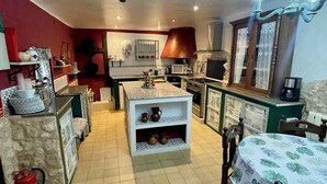 Een compacte keuken met een centraal eiland, een eethoek met tafel, en een rode accentmuur.