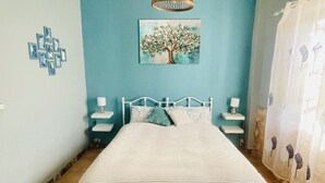 Een slaapkamer met een bed, nachtkastjes, een hanglamp, een schilderij aan de muur en een bankje met handdoeken.