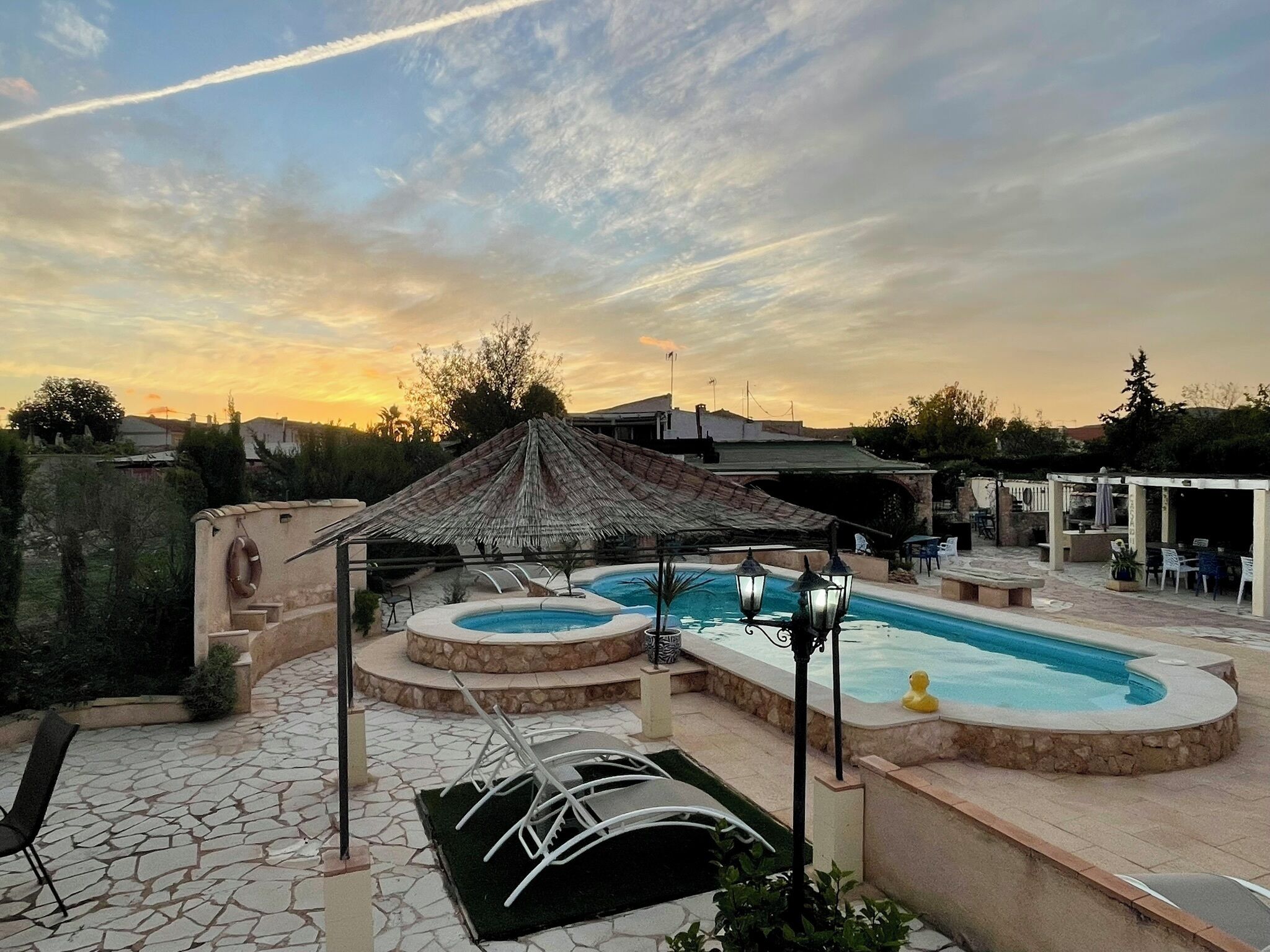 Un patio trasero con piscina, una zona de estar techada y un patio con suelo de piedra.